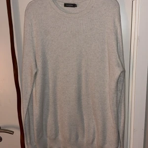 Ljusgrå stickad tröja från Dressmann - En stilren ljusgrå stickad tröja från Dressmann i storlek 2XL. Tröjan har rund halsringning, ribbade muddar och är långärmad. Perfekt för lager-på-lager och enkel att matcha med jeans eller chinos.