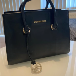 Michael Kors - Michael Kors svart skinnväska Lyxig och stilren med gulddetaljer och MK-logga. Perfekt för vardag eller fest, med rymligt innerfack och dragkedja. Klassisk känsla med modern touch.