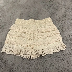 Beige virkade shorts med volanger - Säljer ett par ljusbeige virkade shorts med bred resår i midjan och flera lager volanger. De har ett detaljerat spetsmönster och ger en riktigt söt och bohemisk vibe. Perfekta för varma dagar och festivalhäng. köptes utomlands i somras men aldrig använda då de var lite för lösa på mig, så de är i nyskick!💞