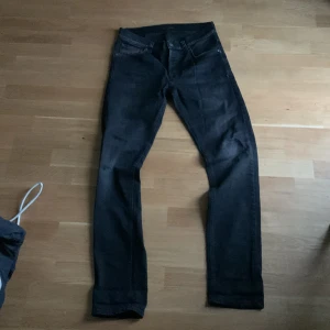 Svarta jeans från Nudie Jeans, 32/34 (Tilted Tor) - Svarta jeans från Nudie Jeans i klassisk rak modell. Jeansen har fem fickor, bälteshällor och subtila sömmar. Tillverkade i slitstarkt jeanstyg med snygg passform. Perfekta för dig som gillar stilrena och tidlösa byxor. Storlek: W32 L34
