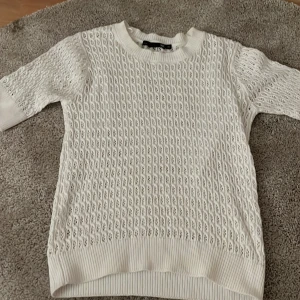 Vit stickad tröja från lager 157 - Säljer en vit stickad tröja från lager 157 med snyggt hålmönster och ribbade muddar. Tröjan har rund halsringning och trekvartsärm, perfekt för lager-på-lager och en fräsch look.
