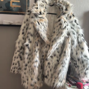 Fluffig pälsjacka med leopardmönster - Säljer en superfluffig pälsjacka i vitt med svarta och beige fläckar som ger en leopardinspirerad look. Jackan har lång ärm, bred krage och är perfekt för dig som vill sticka ut. Fodrad insida för extra komfort och värme. Passar dig som gillar statement-plagg.