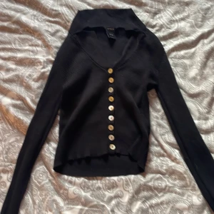 Svart ribbad kofta från Lindex XS - Svart ribbad kofta från Lindex i storlek XS. Koftan har v-ringning, långa ärmar och snygga guldiga knappar hela vägen framtill. Perfekt för lager-på-lager och enkel att styla till olika looks.