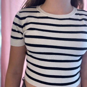 Randig croppad topp från Gina Tricot (Barn) - Säljer en croppad topp från Gina Tricot med svartvita horisontella ränder. Toppen är ribbad, har rund halsringning och korta ärmar. Perfekt för dig som gillar en enkel men snygg stil. Materialet är mjukt och stretchigt för en bekväm passform.
