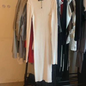 Vit ribbad långklänning - Långärmad vit ribbad klänning med kroppsnära passform och rund hals. Klänningen är hellång och har en stilren, minimalistisk look som passar perfekt för dig som gillar enkel men snygg stil.