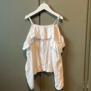 Vit volangtop från H&M med smala band - Säljer en söt vit topp från H&M med smala axelband och volangdetalj över bysten. Toppen har resår upptill och nertill för en skön passform. Perfekt för dig som gillar en luftig och somrig stil. Materialet är mjukt och lätt, materialet är 100% viskos