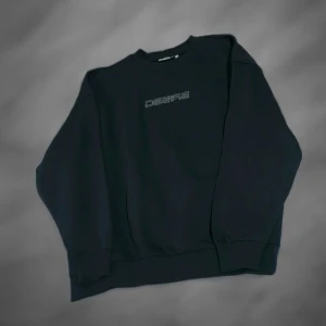 Svart sweatshirt med tryck Desire - Svart oversized sweatshirt med texten 'DESIRE' tryckt på bröstet i vitt. Tröjan har rund halsringning och långa ärmar med breda muddar. Perfekt för en avslappnad och stilren look.