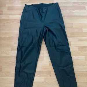 Svarta Skinnimitation från Noisy May - Snygga svarta skinnimitation byxor från Noisy May med smal passform, resår och dragkedja på sidan. Byxorna har hög midja och elastisk linning för extra komfort. Perfekta för dig som vill ha en edgy look med stilren känsla.