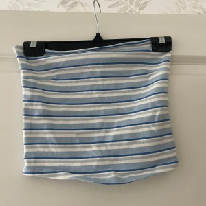 Randig blåvit tubtopp - Säljer en fräsch tubtopp med blå och vita ränder. Toppen är bandeau-modell och har en tight passform. Perfekt för varma dagar och enkel att matcha med jeans eller kjol. Materialet är mjukt och stretchigt för extra komfort.