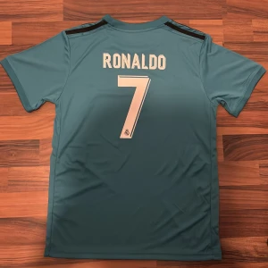 Real Madrid Ronaldo 7 Adidas tröja - Säljer en blå Real Madrid fotbollströja från Adidas med Ronaldo 7 på ryggen. Tröjan har korta ärmar, digitalt pixelmönster i mörkblått framtill, klubbmärke och Fly Emirates-tryck. Tillverkad i lätt och ventilerande ClimaCool-material. Storlek 14-15 år/xs