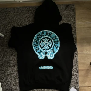 Chrome Hearts svart hoodie med blått tryck - Svart hoodie från Chrome Hearts UEA (sprillans ny med tags kvar) med stort blått tryck på ryggen och mindre tryck på bröstet. Klassisk huva och känguruficka framtill. Grym kvalité dvs inga billiga tyger väger ca 400g! Bara höra av dig om du har några frågor eller vill ha fler bilder! Original paketering finns kvar☺️