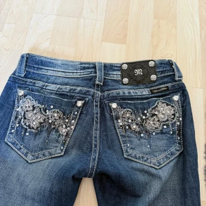 Miss Me jeans  - Snygga blå Miss Me jeans med broderade bakfickor, paljetter och blommiga detaljer. Jeansen har en låg midja samt bootcut/ flate modell och är i strl 26. Skriv privat för mer bilder och mått!
