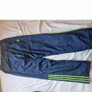 Adidas marinblå träningsbyxor M - Dom kommer inte längre till användning. Dom är väldigt långa så har används hemma inte så många gånger. Snöret i midjan gick sönder så det är ersatt med ett annat. Marinblå träningsbyxor från Adidas med klassiska neongröna ränder längs benen och Adidas-logga på låret. Byxorna har resår och snörning i midjan samt meshfoder på insidan. Perfekta för sport eller chill.