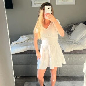 Vit kortklänning från Gina Tricot - Supersöt vit kortklänning från Gina Tricot med v-ringning, smockad midja och volangig kjol finns 2 stycken man får båda på köptet ”om man vill” 💗
