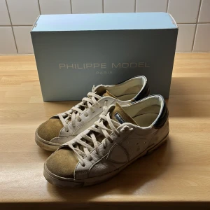 Philippe Model PRSX sneakers, vit/mustard - Snygga Philippe Model PRSX Low Man sneakers i vintage stil. Skorna är vita med senapsgula detaljer och svarta partier vid hälen. Tillverkade i skinn och mocka, med snörning och platt sula. Perfekta för dig som gillar en unik och trendig look. Det är bara att höra av sig vid frågor och funderingar 😀