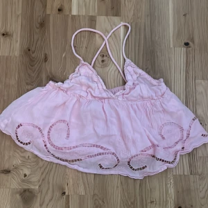 Ljusrosa broderad linnetopp Gina Tricot - Supersöt ljusrosa linnetopp från Gina Tricot med tunna axelband som korsas i ryggen. Toppen har broderade detaljer och utskurna mönster längs nederkanten, samt en luftig och flowy passform. Perfekt för varma dagar och somriga vibes!