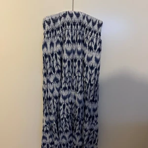Blåvit långkjol med mönster - Säljer en snygg blåvit långkjol med coolt abstrakt mönster. Kjolen har smock upptill, den har en avslappnad och somrig vibe. Perfekt för varma dagar och semester. Materialet känns lätt och luftigt.