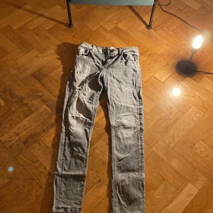 Replay grå jeans med slitningar - Säljer ett par grå jeans från Replay med snygga slitningar på benen. Jeansen har klassisk femficksdesign, raka ben och normal passform. Perfekta för dig som gillar en avslappnad och trendig look. Materialet är jeans och färgen är en tvättad grå nyans.