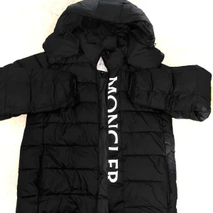 Svart pufferjacka från Moncler sorlek S  - Säljer en svart pufferjacka från Moncler med stor huva och tydlig logga på bröstet. Jackan har quiltad design, dragkedja framtill och Moncler-tryck längs insidan. Perfekt för kalla dagar och riktigt snygg streetstil. Den är störe än vad en riktigt S sorlek så M-L mellan där och en av fikorna har ingen zip men den är i bra skick 