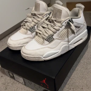 Nike Air Jordan 4 Retro vita sneakers - Säljer ett par Nike Air Jordan 4 Retro pure money i helvitt skinn med meshpaneler och coola metalliska detaljer vid snörningen. Klassisk Jumpman-logga på hälen och platt sula. Perfekta för dig som gillar streetstyle och vill sticka ut med en ikonisk sneaker.