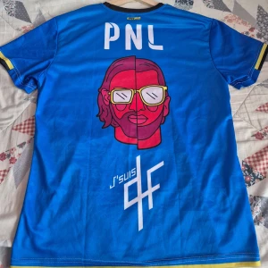 PNL 90 minutes jersey  - Snygg blå jersey från PNL med coolt grafiskt tryck både fram och bak, inklusive texten 'Que La Mif' och unika illustrationer. T-shirten har korta ärmar med svarta och gula detaljer vid mudden och är gjord i mjukt polyester-material.