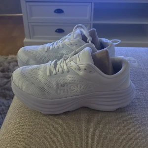 Vita Hoka skor  - Säljer ett par helvita Hoka sneakers med riktigt chunky sula och ventilerande mesh-ovandel. Skorna har snörning och en modern, sportig look med Hoka-logga på sidan. Perfekta för dig som gillar stilrena och bekväma sneakers med extra dämpning. HELT NYA ENDAST TESTADE!
