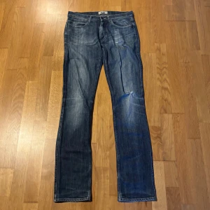 Blå raka jeans från Acne - Snygga blå jeans från Acne med klassisk femficksdesign och raka ben. Jeansen har en mellanblå tvätt med diskreta slitningar och tydliga sömmar. Tillverkade i jeansmaterial med normal passform och midja. Perfekta för en stilren och avslappnad look.