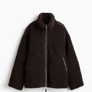 Brun teddyjacka med dragkedja/ pilejacka - Mysig brun teddyjacka med hög krage och hel dragkedja framtill. Jackan har två stora fickor med detaljer i skinnimitation och en loose passform. Prislappen är kvar och är aldrig använd, den är slutsåld på hemsidan.🫶🏽🤎 storlek L och priset kan diskuteras.🩷