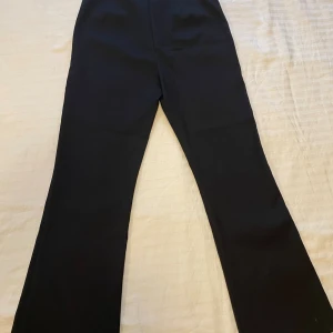 Svarta kostymbyxor från Zara - Stilrena svarta kostymbyxor från Zara med klassisk passform och raka ben. Byxorna har hög midja, diskreta fickor och stängs med både hake och dragkedja. Perfekta för en clean och snygg look. Materialet är mjukt och följsamt.