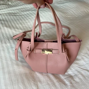 Rosa handväska i skinn med gulddetalj - Jättefin rosa väska från Lindex. Slutsåld och populär!! Använd en gång så den är som ny