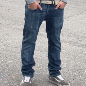 Levi's 511 blå jeans W32 L32 - Snygga Levi's 511 jeans i klassisk blå tvätt med diskreta slitningar. Modellen är slim och har raka ben, fem fickor och detaljerade sömmar. Jeansen är tillverkade i bomull och har en ikonisk läderpatch bak i midjan. Perfekta för en avslappnad och stilren look.