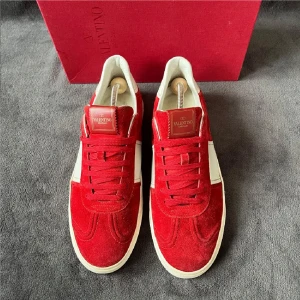 Valentino Garavani röda sneakers mocka - Riktigt snygga Valentino Garavani sneakers i röd mocka med vita skinnpaneler och vita sulor. Skorna har snörning, rund tå och coola nitar på hälen. Perfekta för dig som vill sticka ut med exklusiva och trendiga sneakers.