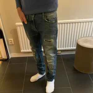Tiger of Sweden jeans med slitningar - Snygga blå slim fit jeans från Tiger of Sweden i modellen pistolero , med coola slitningar och tvättade detaljer på benen. Klassisk femficksmodell, orange sömmar och läderpatch bak i midjan. Jeansen är slim i modellen och tillverkade i bomull.