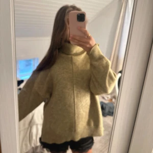 Beige stickad polotröja - Mysig beige stickad polotröja med oversized passform och lång ärm. Tröjan har en hög krage och synlig söm framtill som ger en cool detalj. Perfekt för lager-på-lager under kyliga dagar.