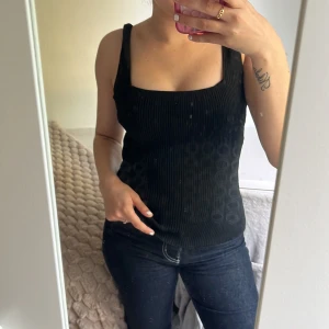 Svart ribbad linnetopp - Säljer en svart ribbad linnetopp med breda axelband och fyrkantig urringning. Toppen är figurnära och har en stilren look som passar perfekt till jeans eller kjol. Materialet är stretchigt och bekvämt, vilket gör den enkel att bära hela dagen.