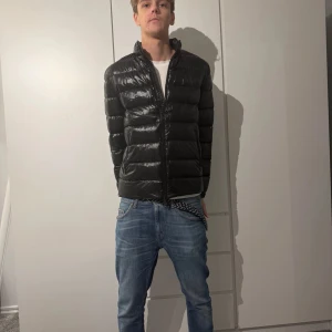 Svart pufferjacka från Massimo dutti  - Säljer en svart, glansig pufferjacka med hög krage och hel dragkedja framtill. Jackan har en clean look med horisontella sömmar och sitter snyggt på kroppen. Perfekt för kyligare dagar och passar till det mesta. Köp nu så skickar jag idag, priset sänks till 150