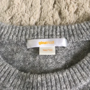 Grå croppad stickad tröja Gina Tricot - Supermjuk och croppad grå stickad tröja från Gina Tricot. Tröjan har korta ärmar, rund halsringning och ribbade kanter. Perfekt att styla med jeans för en chill look.