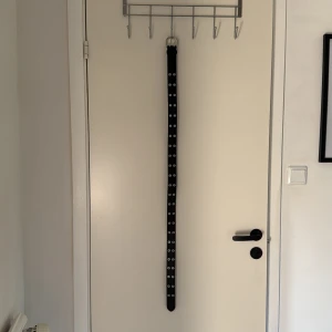 Svart bälte/skärp - Snyggt svart bälte med dubbla rader av silverfärgade metallhål längs hela längden. Bältet har en klassisk, rundad spänne i silver och är tillverkat i skinnimitation. Perfekt för att ge din outfit en edgy vibe och passar till jeans eller kjol.🫦 Använd endast en gång, så är i väldigt gott skick!
