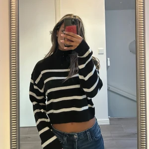 Svartvit randig croppad stickad tröja - Säljer en svart och vit randig croppad stickad tröja med polokrage. Tröjan har långa ärmar och en loose passform, perfekt för dig som gillar en avslappnad stil. Snygg att matcha med jeans eller kjol.