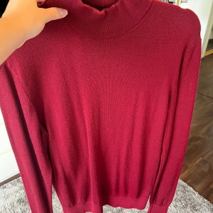 Vinröd polotröja med ribbad krage - Snygg vinröd polotröja med ribbad hög krage och långa ärmar. Tröjan är stickad i ett mjukt material och har ribbade muddar vid ärmslut och nederkant. Märke Jerem black collection