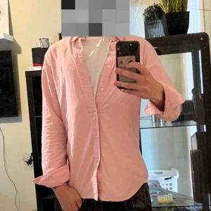 Rosa skjorta från Ralph Lauren - Säljer en klassisk rosa skjorta från Ralph Lauren med broderad logga på bröstet. Skjortan har lång ärm, knappar framtill och är gjord i mjuk bomull. Perfekt för dig som vill ha en clean och stilren look.