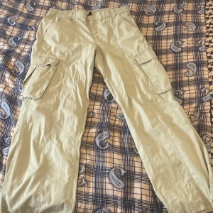 Beiga cargobyxor från H&M, strl 42 - Snygga beiga cargobyxor från H&M i storlek 42. Byxorna har flera stora fickor på sidorna och resår i midjan för extra komfort. Tillverkade i 100% bomull, perfekta för en avslappnad och cool stil.