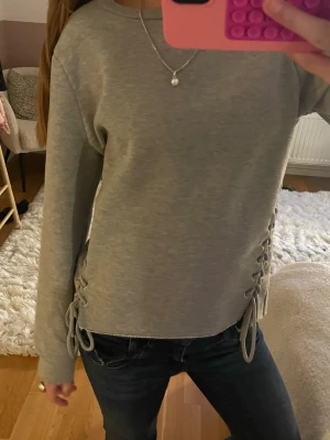 Grå tröja med snören - Såå cool och unik!! Köpte på sellpy men helt oanvänd🙌🏼🙌🏼💕står inte storlek men skulle gissa på s, jag är 1,64 m!!