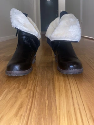 Vinterskor, Svarta boots med vit fuskpäls - Säljer ett par svarta boots med vit fuskpälsfoder och dragkedja på sidan. Skorna har rund tå och platt sula, tillverkade i skinnimitation med grov yttersula. Perfekta för kalla dagar och har en snygg kontrast mellan det mörka och ljusa. Pris går att diskuteras bara vid snabba köp! 🤩❤️