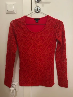 Röd spetsblus från Amisu XS - Säljer en röd långärmad blus från Amisu i storlek XS. Toppen har ett genomgående blommigt spetsmönster på framsidan och ärmarna, medan ryggen är slät. Rund halsringning och figurnära passform. Perfekt för dig som gillar detaljer och färg.🌹❤️