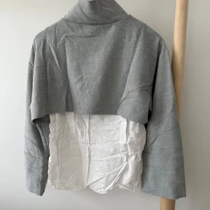 Grå croppad tröja från Zara Trafaluc - Unik croppad tröja från Zara Trafaluc i grått och vitt. Tröjan har hög krage, lång ärm och cool dragkedja längs axeln. Oversized fit och blandat material med bomullskänsla. 