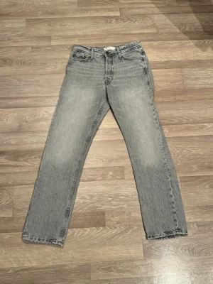 Grå loose fit jeans från Jack & Jones - Säljer ett par grå jeans från Jack & Jones med loose fit och raka ben. Jeansen har klassisk femficksdesign, ljus tvätt och tydliga sömmar på bakfickorna. Materialet är bomull och jeans, perfekt för dig som gillar avslappnad stil.
