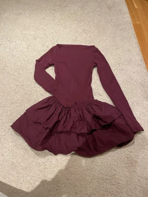 Vinröd volangklänning från Zara - Supersnygg vinröd kortklänning från Zara med långa ärmar och dubbla volanger i kjolen. Klänningen har en tight passform upptill och en fluffig kjol som ger en riktigt cool siluett. Perfekt för dig som vill sticka ut lite extra!