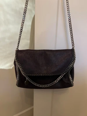Svart axelväska Stella McCartney-liknande - Säljer en svart axelväska  Stella McCartney-liknande med kedjedetaljer runt kanterna och som axelrem. 