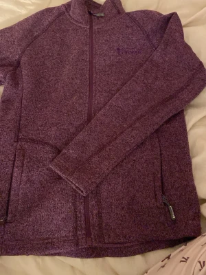 Lila stickad kofta från Pinewood - Mysig lila kofta från Pinewood Outdoor Collection med hel dragkedja framtill och två sidofickor med dragkedja. Stickad känsla och hög krage som håller dig varm under kyliga dagar. Perfekt för dig som gillar outdoor och vill ha en snygg och funktionell tröja.